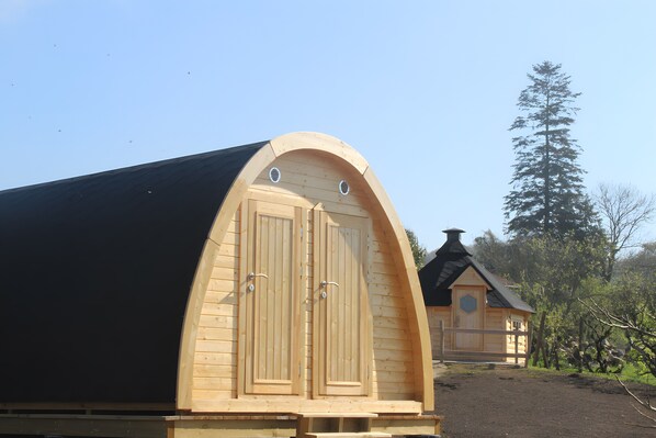 Una cabaña de madera con techo curvo, una chimenea y una puerta con dos ventanas.