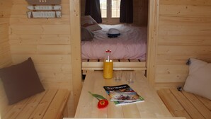 A wooden cabin room with a bed, a table with a bottle, glasses, a book, and a red flower. - Unique Barrel So'Happy - A Gourmet Getaway (Sevremont)