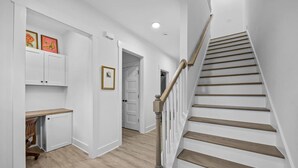 A hallway with a wooden staircase, white walls, and a door leading to another room. - Modern New Duplex in Prime Location (Haw River)