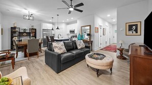 A modern living room with a dark sofa, a wooden coffee table, and a TV stand. There is a dining area with a table and chairs, and a kitchen in the background. - Modern New Duplex in Prime Location (Haw River)