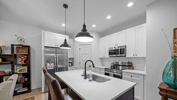 A modern kitchen with white cabinets, stainless steel appliances, and a central island with a sink. - Modern New Duplex in Prime Location (Haw River)
