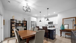 A modern kitchen with white cabinets, a central island, and pendant lighting. - Modern New Duplex in Prime Location (Haw River)