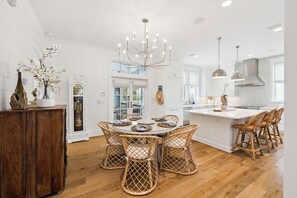 A modern kitchen with a central island, white cabinetry, and a dining area with wicker chairs.