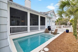 A pool with a covered patio, outdoor furniture, and a white fence.