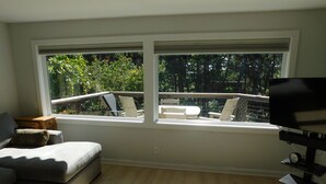 Un salon moderne avec une grande fenêtre, un canapé gris, une table basse en bois et un téléviseur posé sur un meuble.