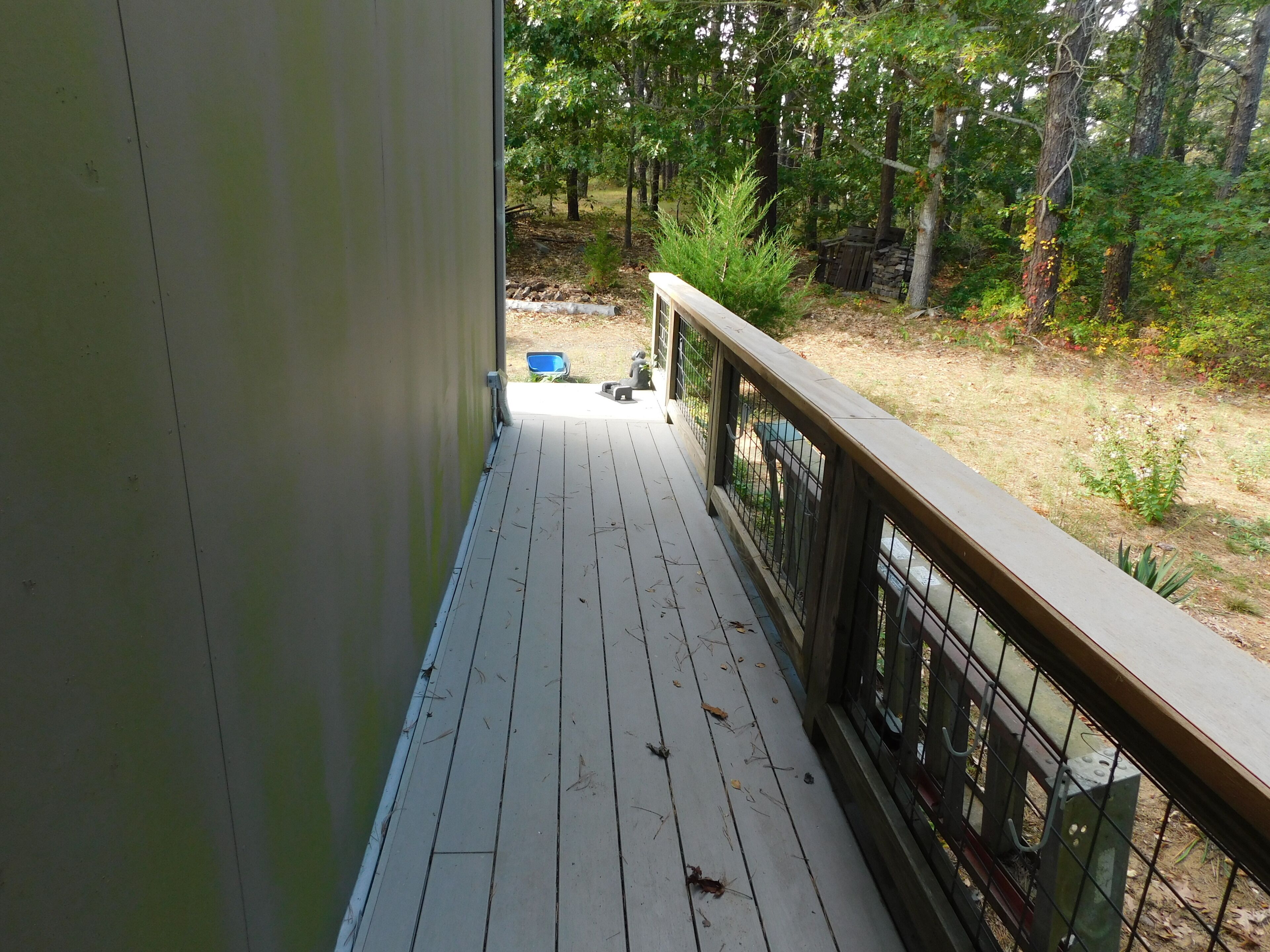 A wooden deck with a metal railing, leading to a grassy area with trees and a blue chair.