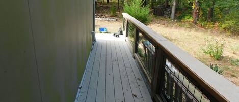 A wooden deck with a metal railing, leading to a grassy area with trees and a blue chair.