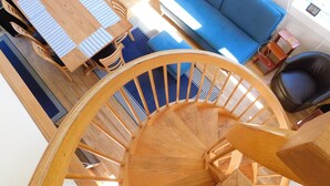 Un escalier en colimaçon en bois donnant sur un coin repas et un canapé bleu.