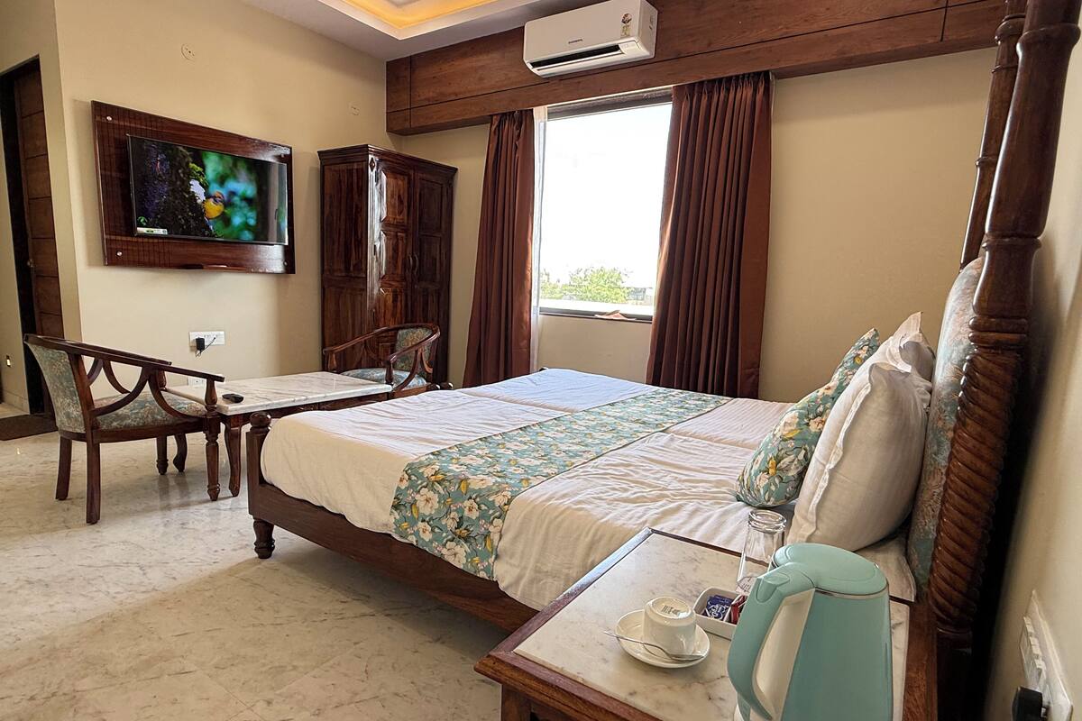 A hotel room with a bed, a desk with a chair, a TV, and an air conditioning unit.