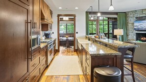 A modern kitchen with wooden cabinets, granite countertops, and a stone fireplace. - Arrowleaf Lodge at Deer Valley Resort - Three Bedroom Residence #203 3 Condo (Park City)