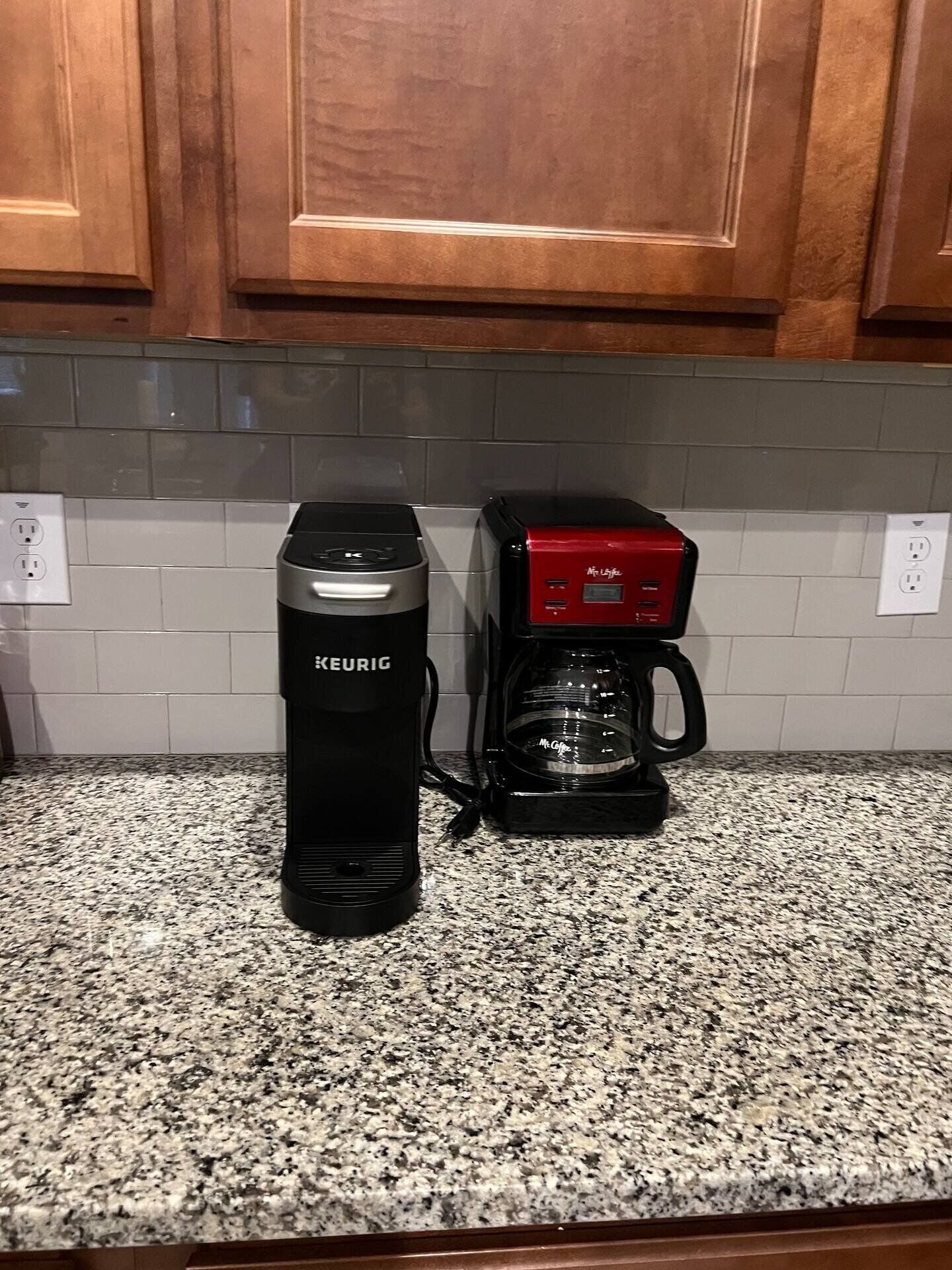 Une cuisine avec une machine à café Keurig noire et une machine à café Mr. Coffee rouge, toutes deux posées sur un comptoir en granit.