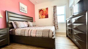 Un dormitorio con cama, cómoda, una pared con un letrero que dice 'Live Simply' y un cuadro con flores.