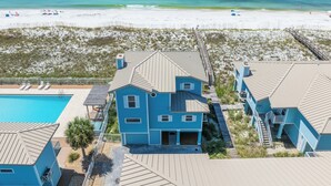 Una propiedad frente a la playa con piscina, playa con sombrillas y un paseo marítimo que conduce a una casa con vistas al océano.