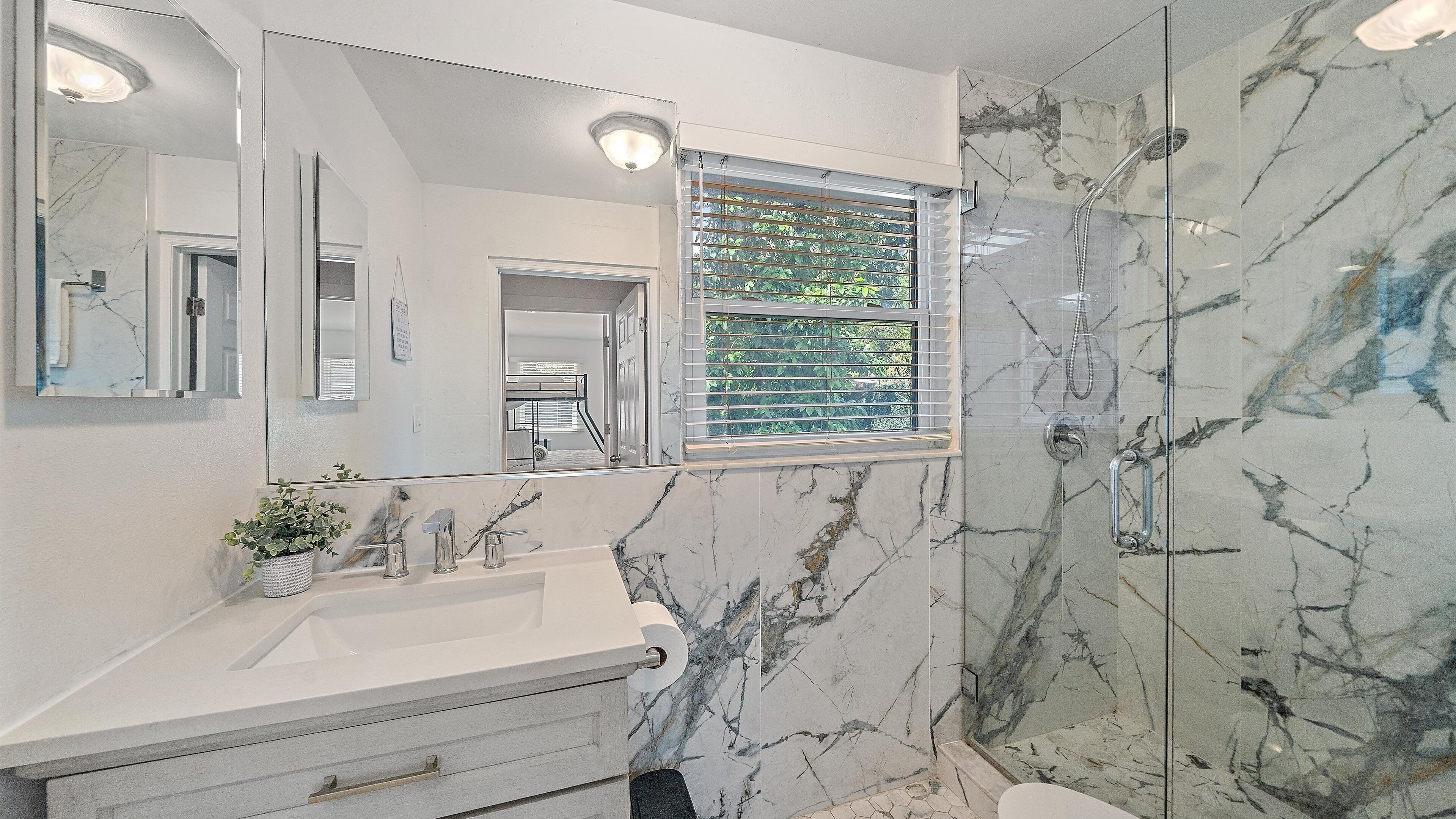 Un baño con pared de mármol, un espejo grande, un lavabo y zona de ducha.