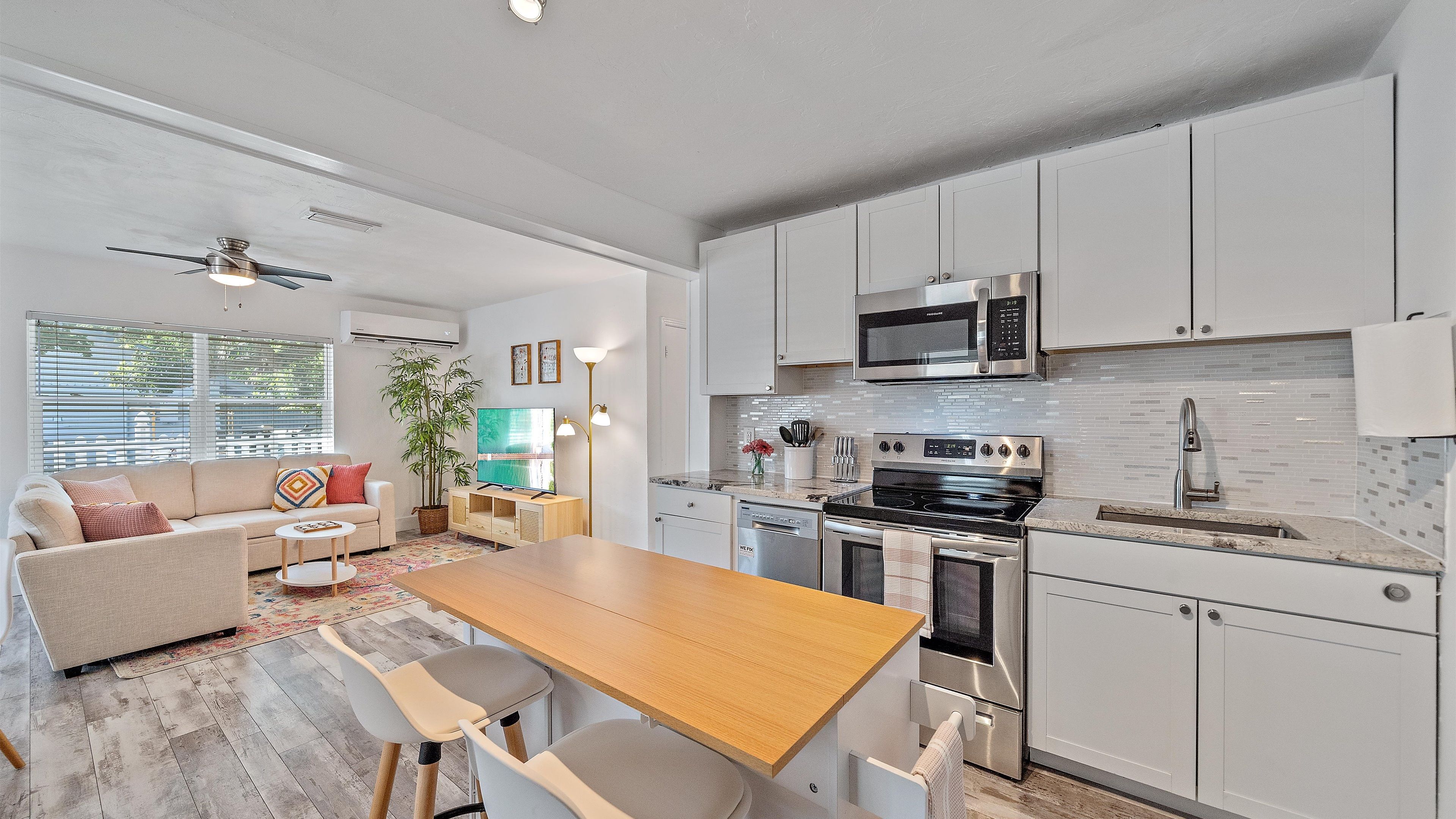 A modern kitchen with white cabinets, a microwave, stove, and dishwasher. There is a dining area with a wooden table and chairs.