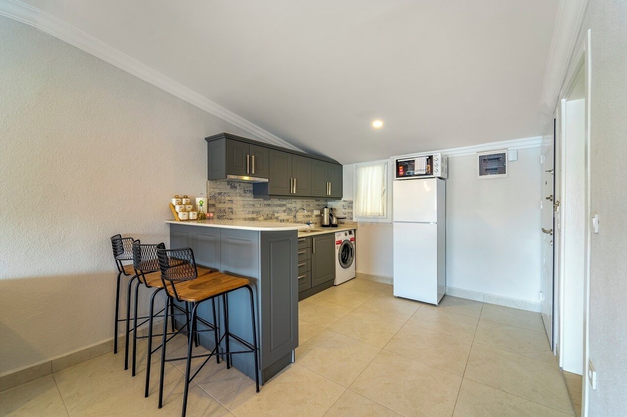 Una cocina compacta con una isla central, taburetes de bar, lavadora y refrigerador.