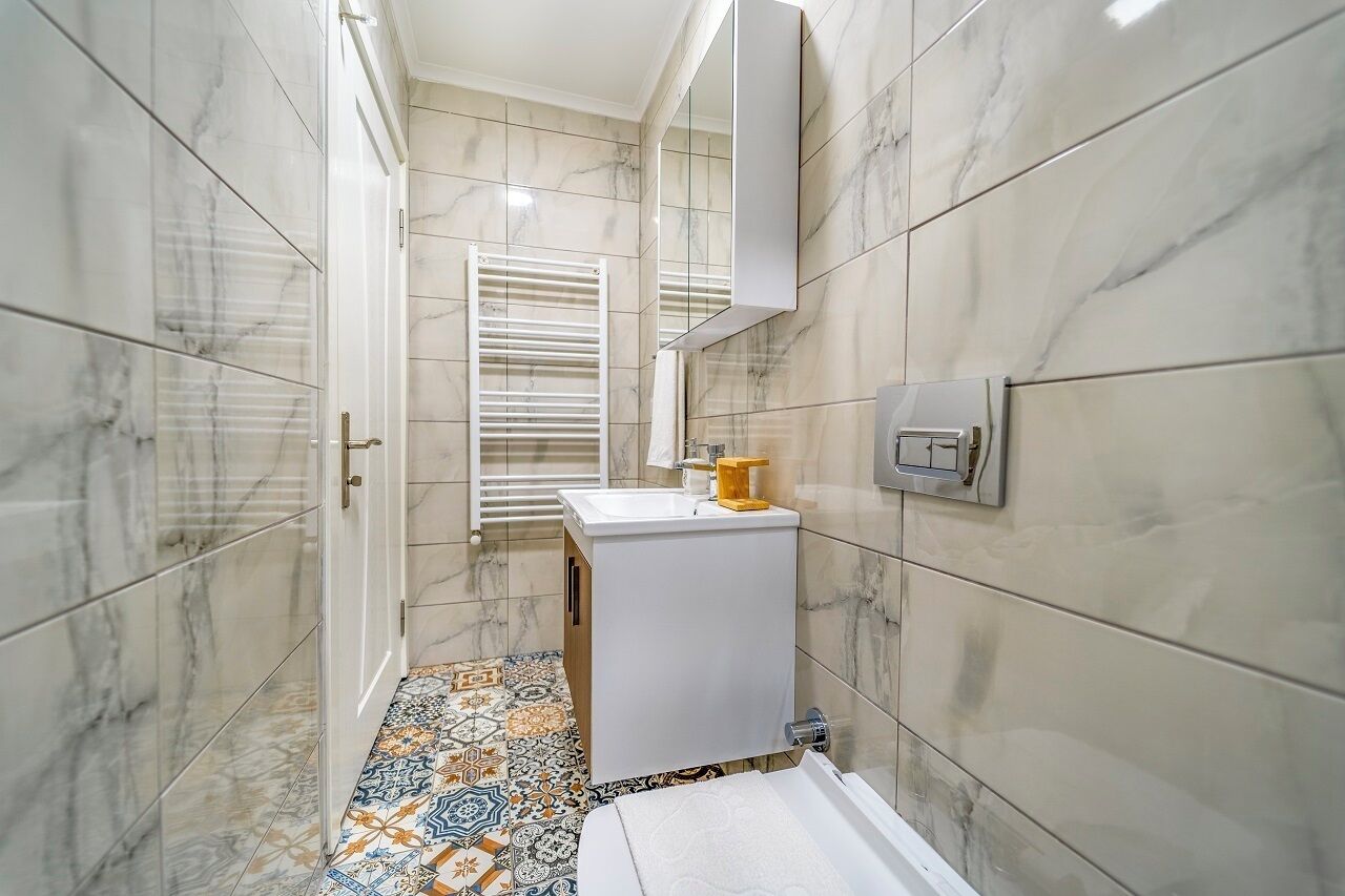 A bathroom with marble walls, a tiled floor, a sink, a mirror, and a towel rack.