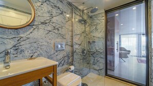 Ein Badezimmer mit Marmorwand, einem Holzwaschtisch, einer Duschkabine und einem großen Fenster.