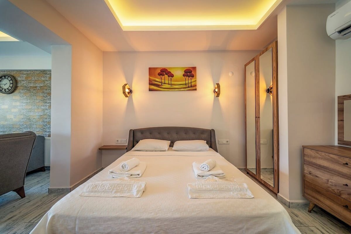 A hotel room with a bed, bedside tables, a clock on the wall, a painting, and a wardrobe.