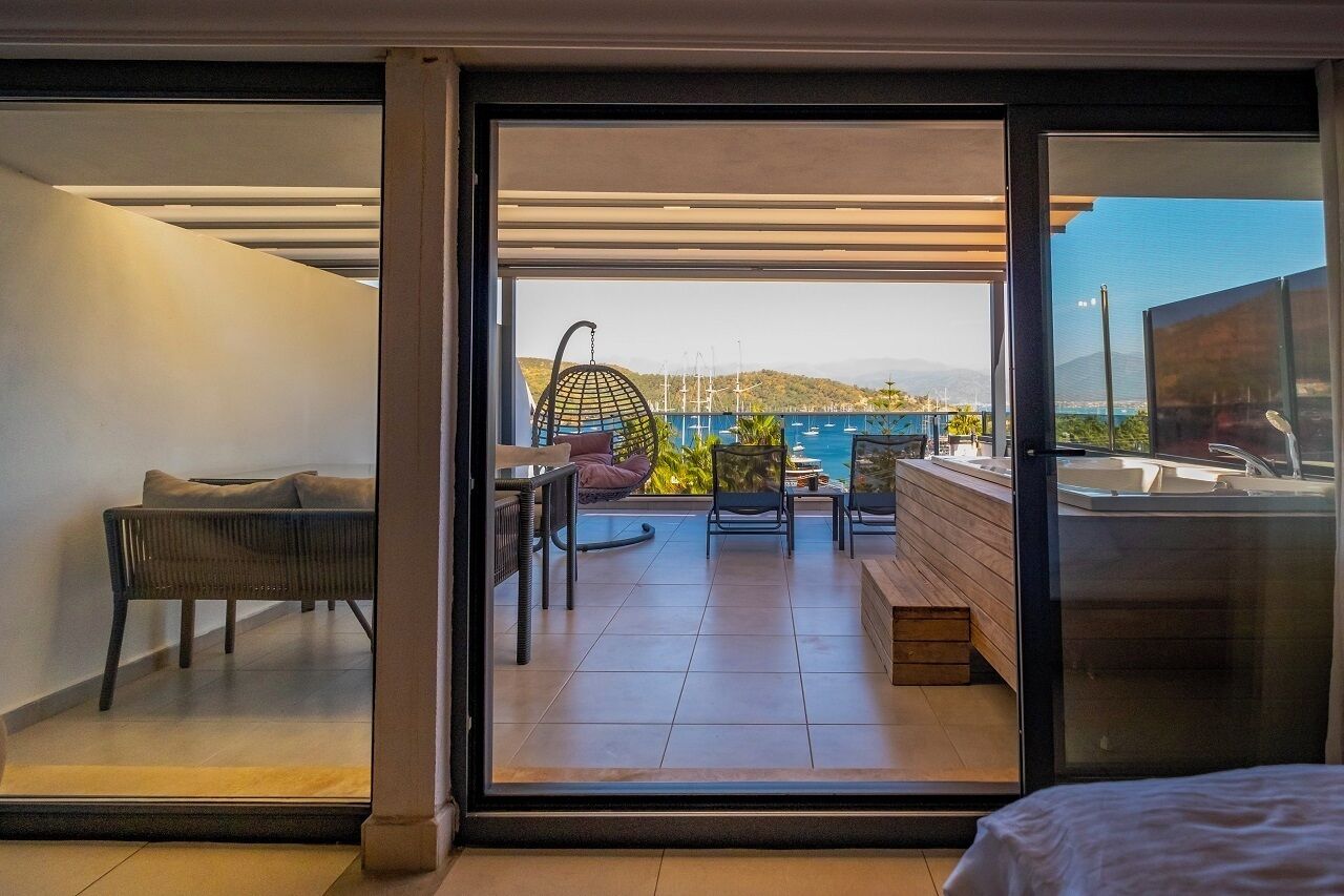 A modern room with a sliding glass door leading to a balcony with a view of the sea and mountains.