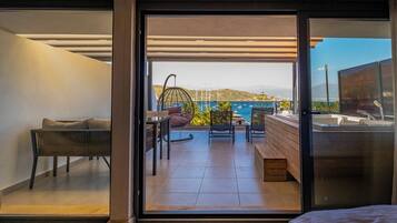 A modern room with a sliding glass door leading to a balcony with a view of the sea and mountains.