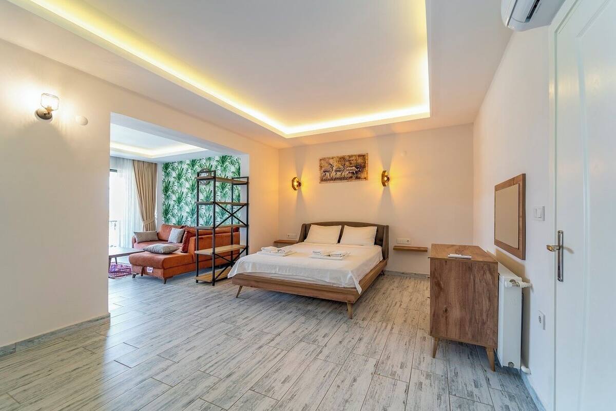 A modern bedroom with a bed, a wooden nightstand, a desk, and a wall-mounted TV.