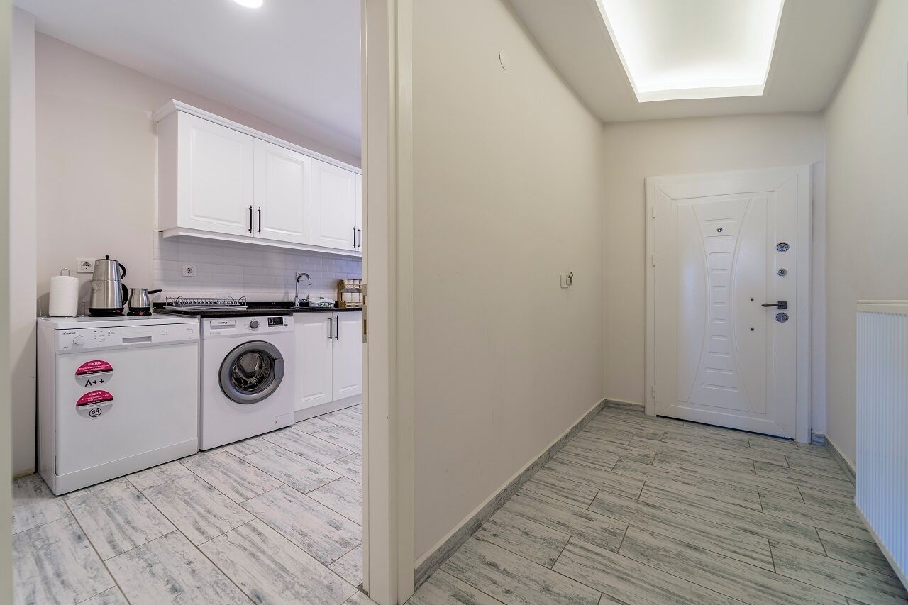 A compact kitchen with white cabinets, a washing machine, and a coffee maker.