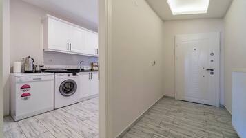 A compact kitchen with white cabinets, a washing machine, and a coffee maker.