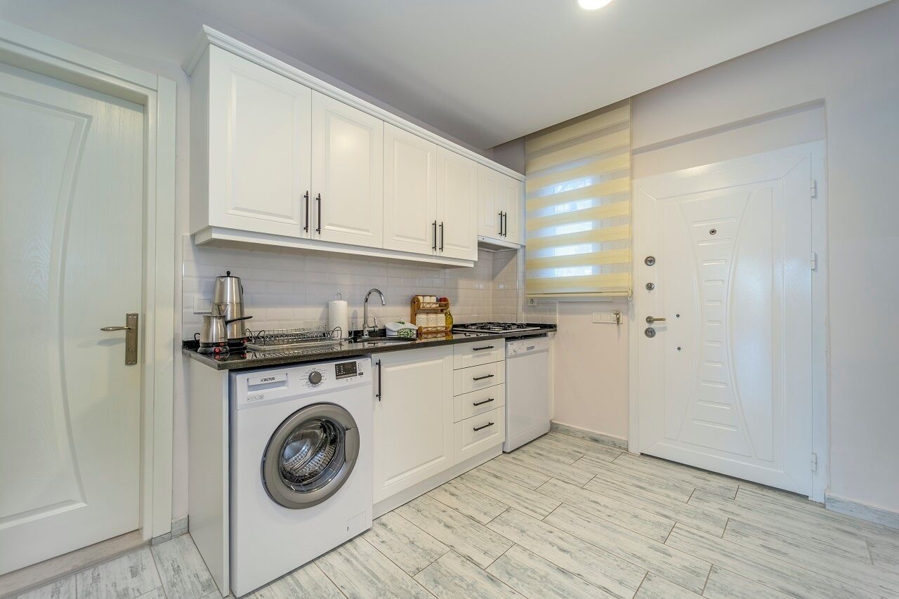 A compact kitchen with white cabinets, a washing machine, and a countertop with various appliances.