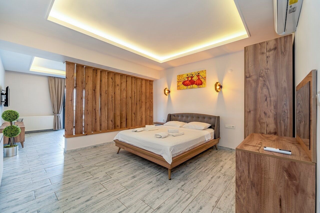 A modern bedroom with a wooden bed, a nightstand, a wall-mounted TV, and a ceiling light fixture.