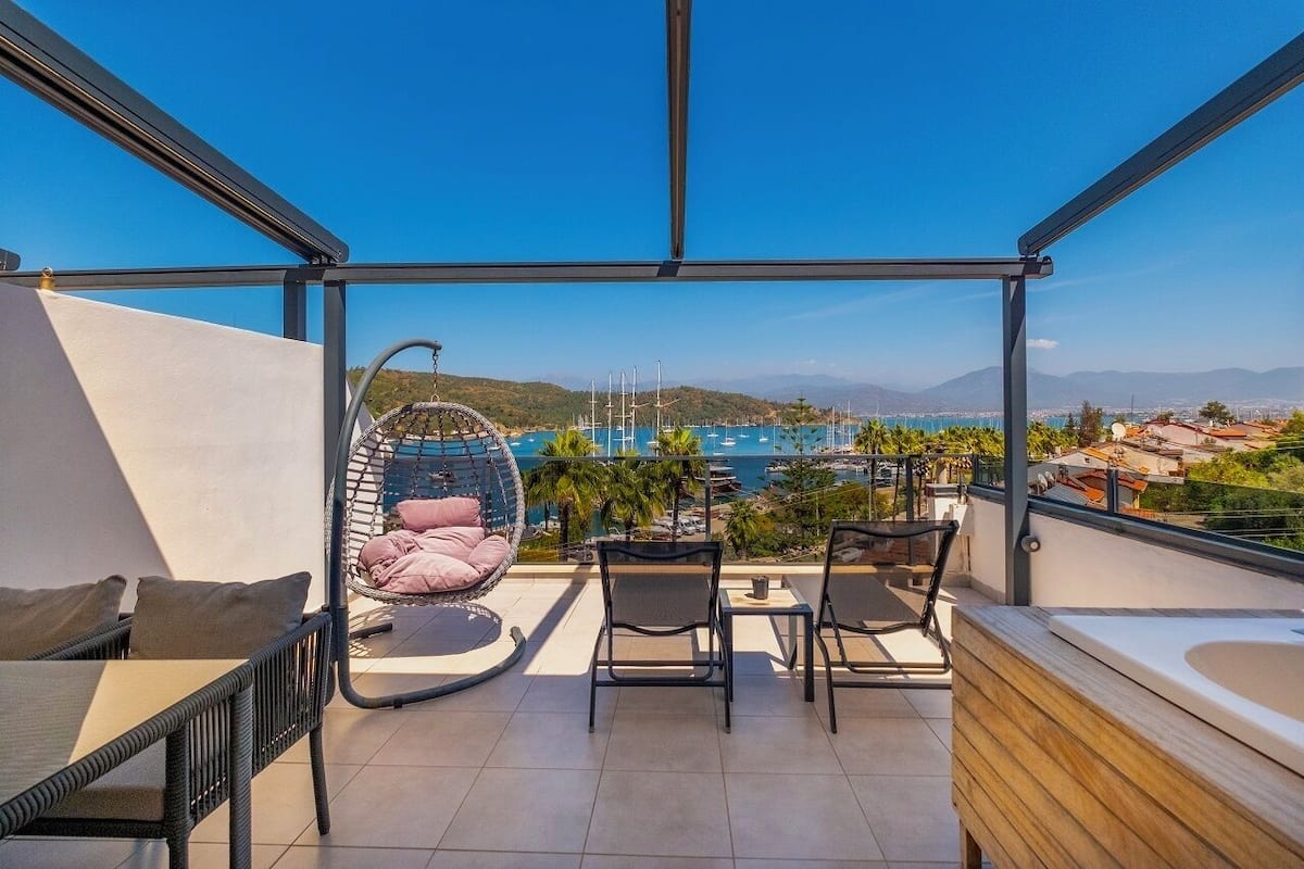 A balcony with a hanging chair, a table, and a bathtub.