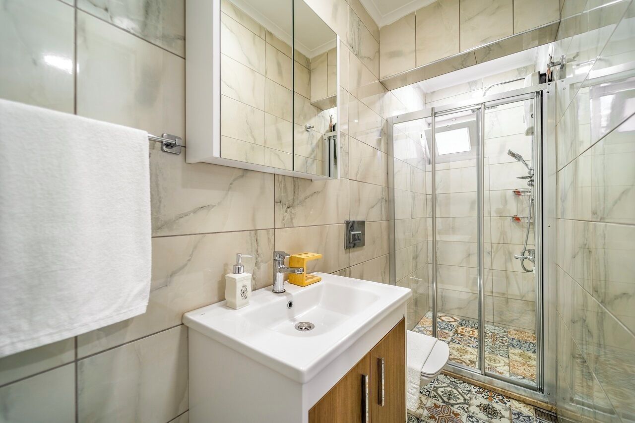 Un baño moderno con lavamanos de mármol, cabina de ducha con paredes de cristal y suelo de baldosas.