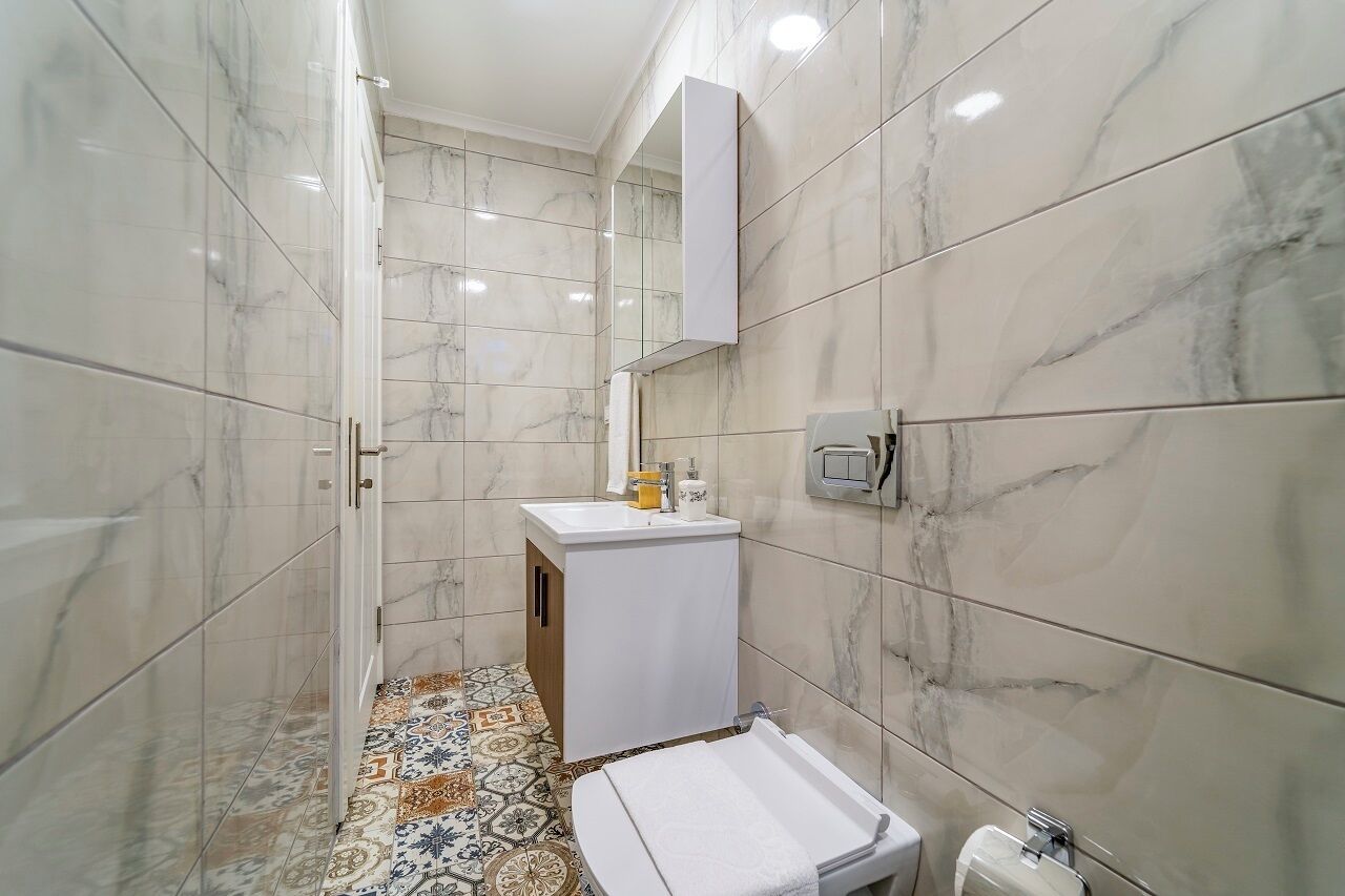 Casa de banho com azulejos de mármore branco, uma pia branca e um espelho.