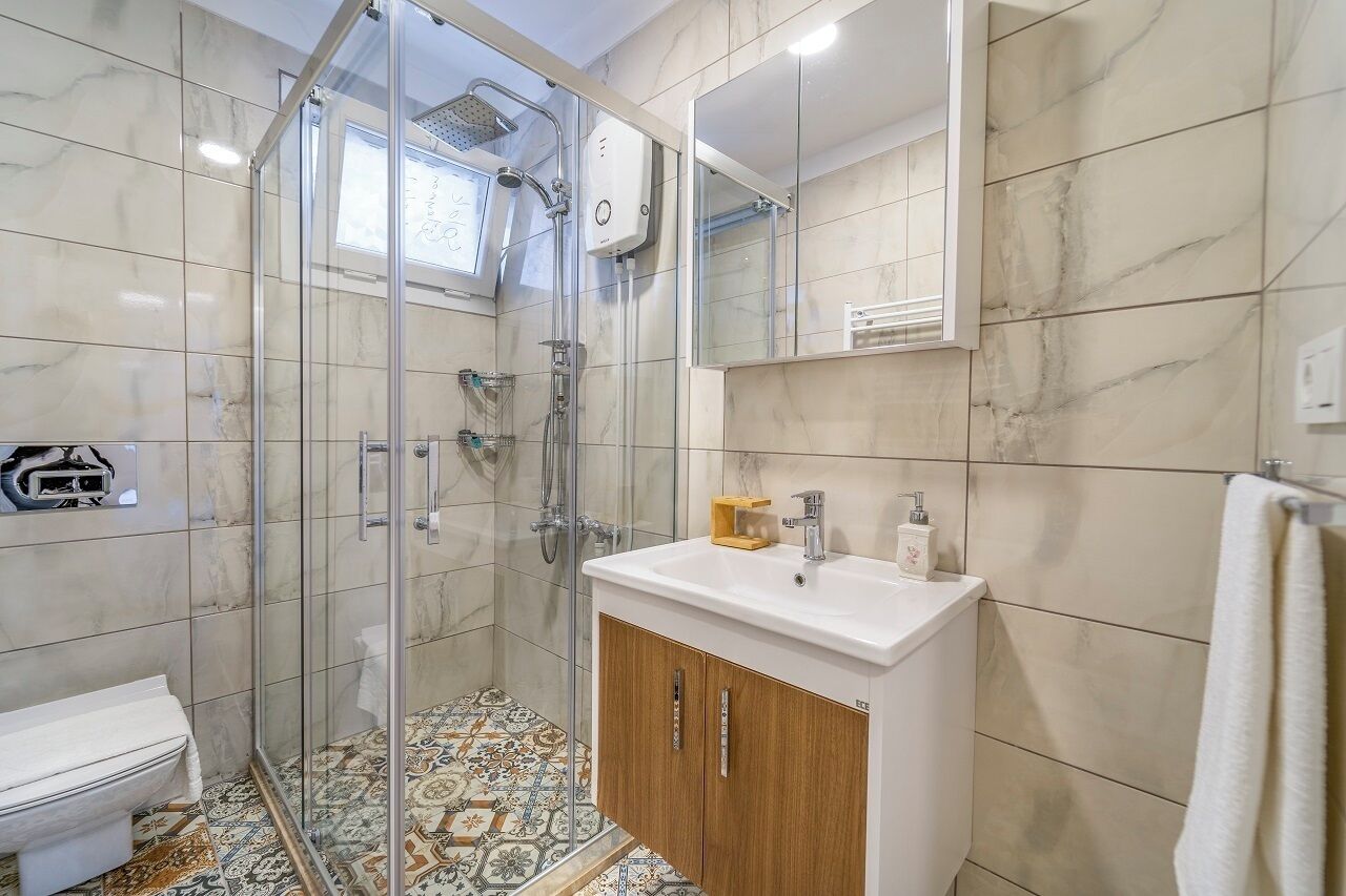 A modern bathroom with a glass-enclosed shower, a white sink with wooden cabinets, and a tiled floor.