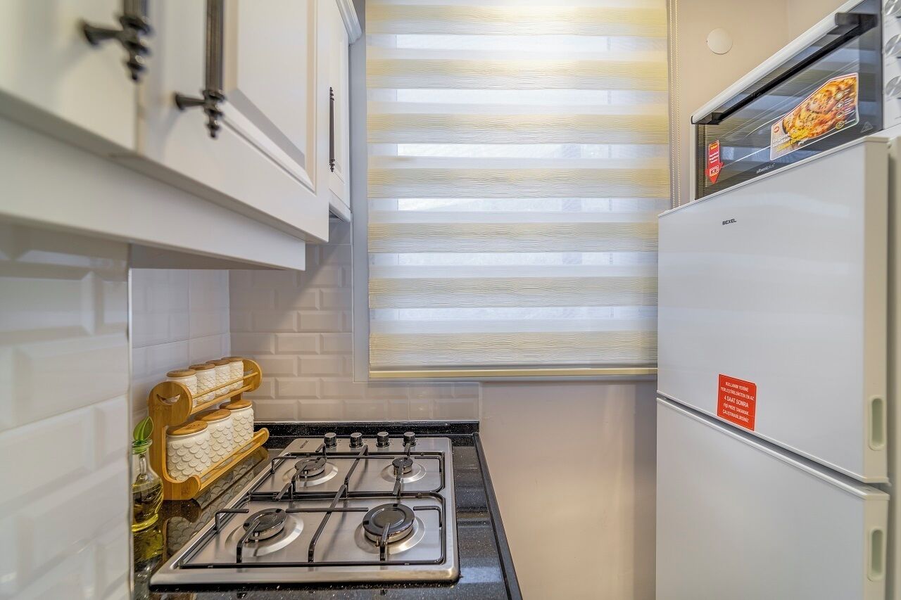 A compact kitchen with white cabinets, a gas stove, and a refrigerator.