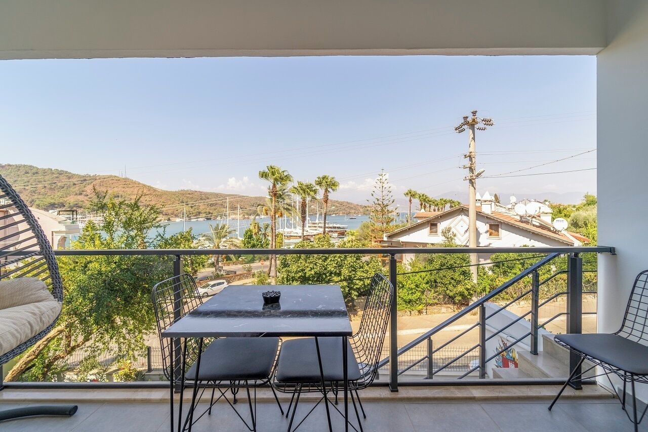 A balcony with a table and chairs, overlooking a marina with boats and palm trees.