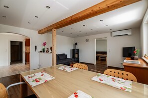 A modern kitchen with wooden beams, a dining area with a table set for four, and a living area with a sofa and TV.