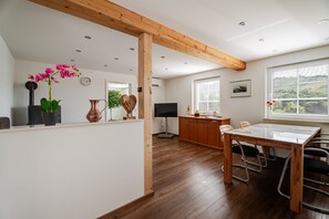 A modern kitchen with wooden beams, a dining area with a table and chairs, and a large window with blinds.