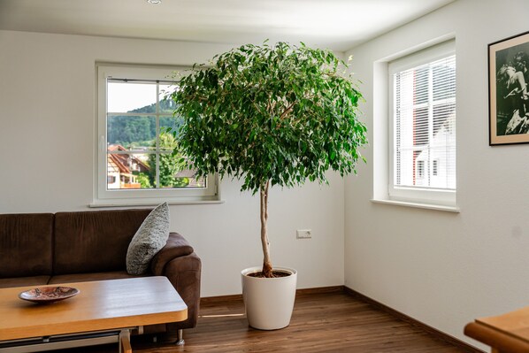 A room with a brown leather sofa, a wooden coffee table, a potted tree, and a framed picture on the wall.
