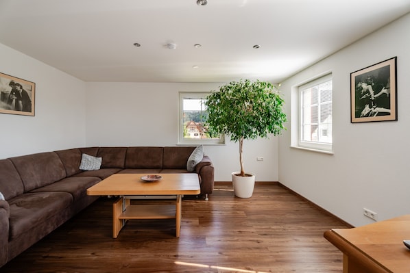 Ein modernes Wohnzimmer mit einer braunen Ledersofa, einem Holztisch, einer Zimmerpflanze und zwei gerahmten Bildern an den Wänden.