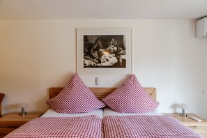 Una habitación de hotel con cama, dos mesitas de noche, lámpara, aire acondicionado instalado en la pared y un cuadro enmarcado.