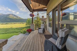 Une terrasse en bois avec des sièges d’extérieur, un jardinier en pierre orné de fleurs et une vue sur les montagnes.