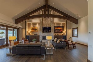 Un salon spacieux doté d’une cheminée en pierre, de poutres en bois foncé et de meubles modernes.