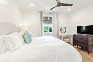 Ein Schlafzimmer mit einem großen Bett, einem Deckenventilator, einem Fernseher und einem Fenster mit Vorhängen.