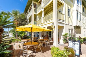 An outdoor patio with yellow umbrellas, tables, and chairs, surrounded by palm trees and a building with balconies. - Seagrove "Beachbound" 1BR, Sleeps 4, Gulf Views, Private Beach Access (Santa Rosa Beach)