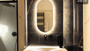 Une salle de bain dotée d’un meuble-lavabo moderne, d’un grand miroir avec éclairage intégré et d’un porte-serviettes noir.