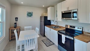 A modern kitchen with white cabinets, a stainless steel refrigerator, a microwave, and an oven. There is a dining table with chairs and a coffee machine on a small table. - Blue Marlin #11 | Bay Views, Community Pool (Rockport)