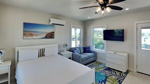 A modern bedroom with a large bed, a ceiling fan, a TV, and a view of the outdoors through the windows. - Blue Marlin #11 | Bay Views, Community Pool (Rockport)