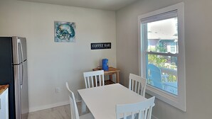 Une cuisine avec une table et des chaises blanches, un réfrigérateur, un panneau indiquant un coin café, et une fenêtre donnant sur un beau paysage.