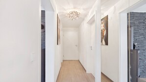 Ein Korridor mit Holzboden, weißen Wänden, einer Deckenleuchte und einem Kühlschrank.